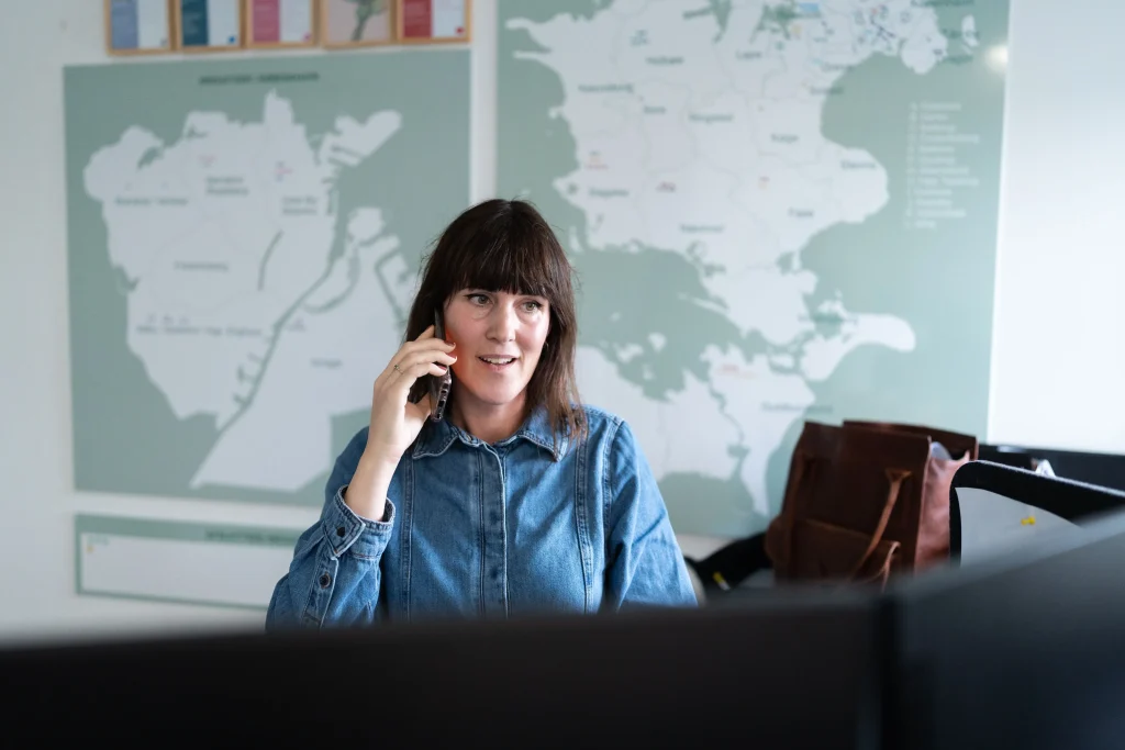 Kvinde taler i telefon på kontor foran vægkort.